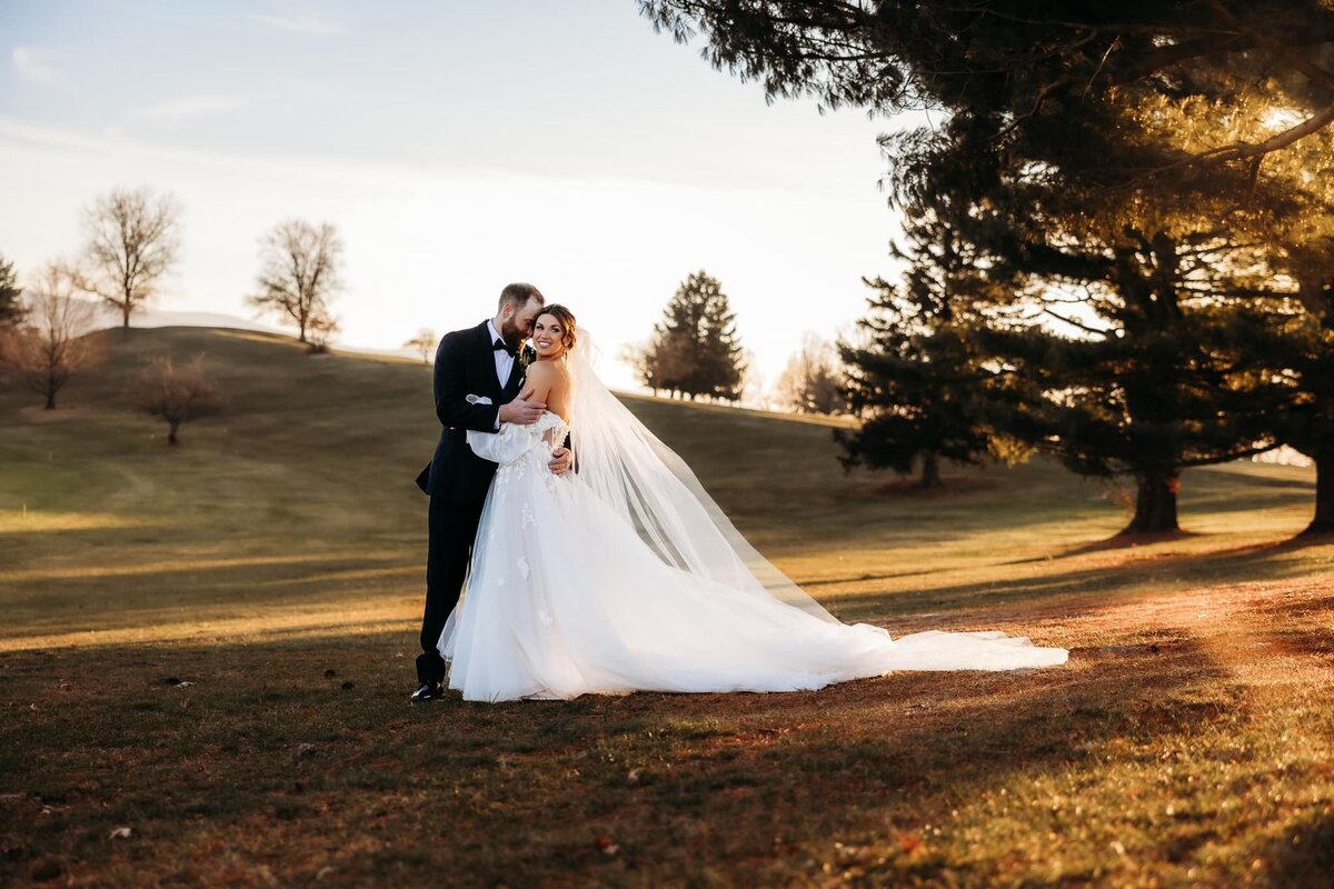 a woman and a man hold hands in wedding attire while standing in a field during the day - photo by Kay Dargen Photography