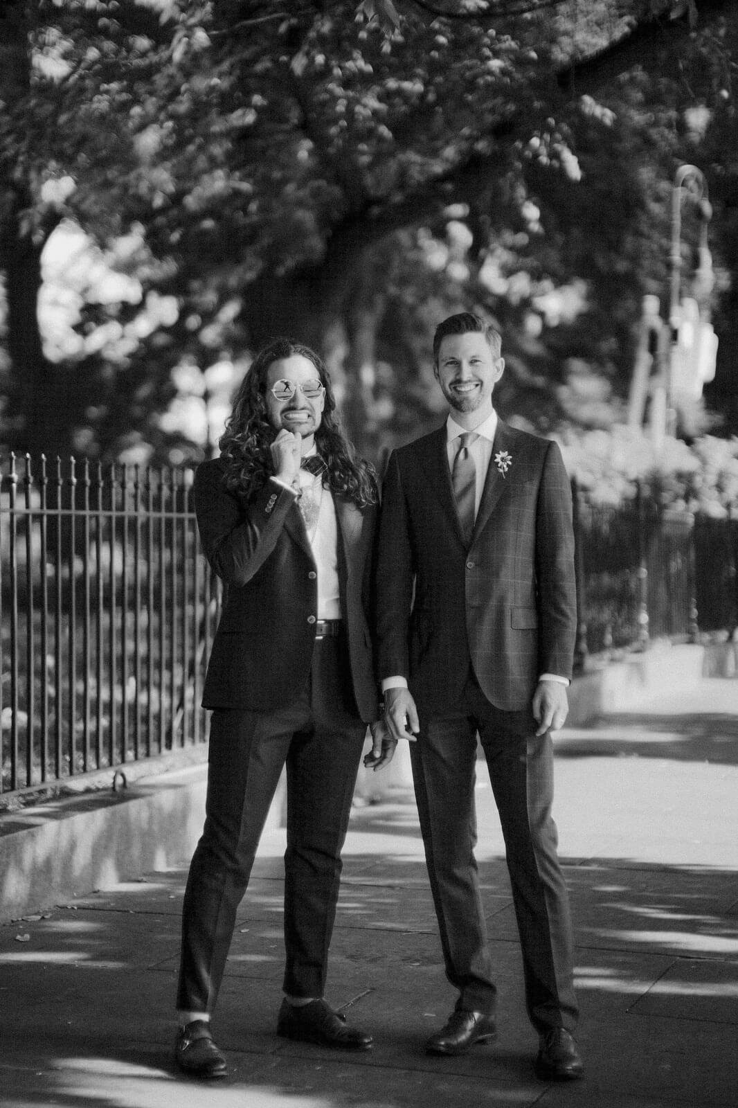 Black and white photo of the two grooms in a park, with trees in the background. NYC City Hall Elopement Image by Jenny Fu Studio