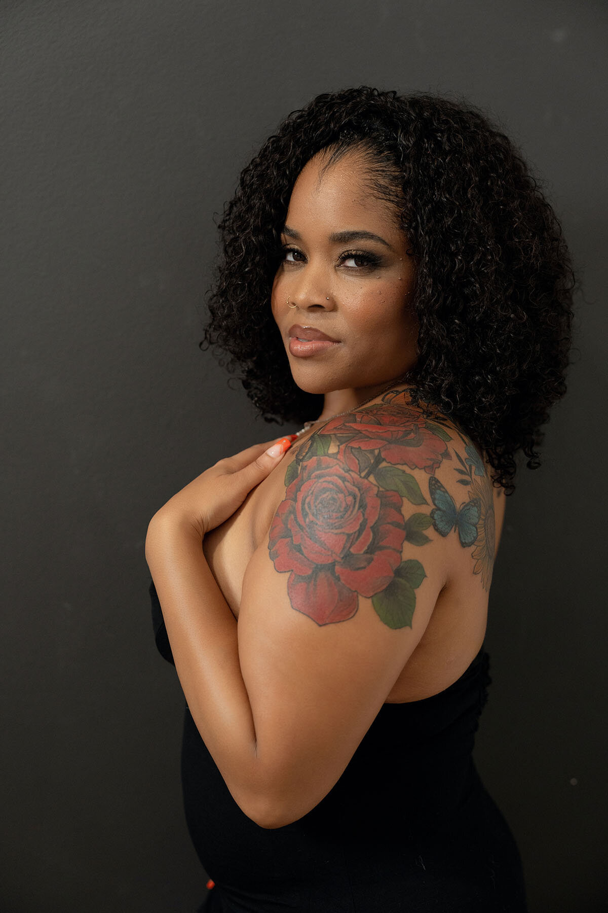 Dark skinned woman with tattoos posing against black backdrop