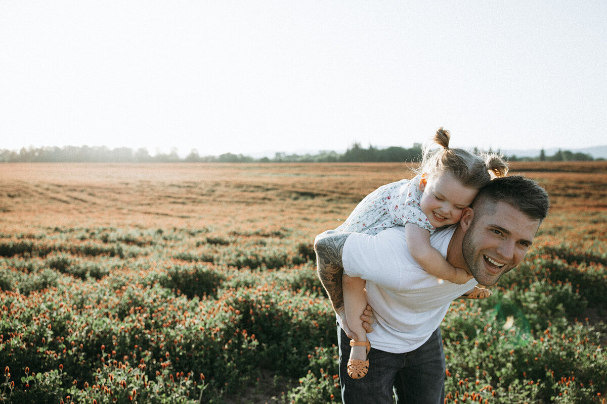 Father gives his little girl a piggy back ride while they both laugh.