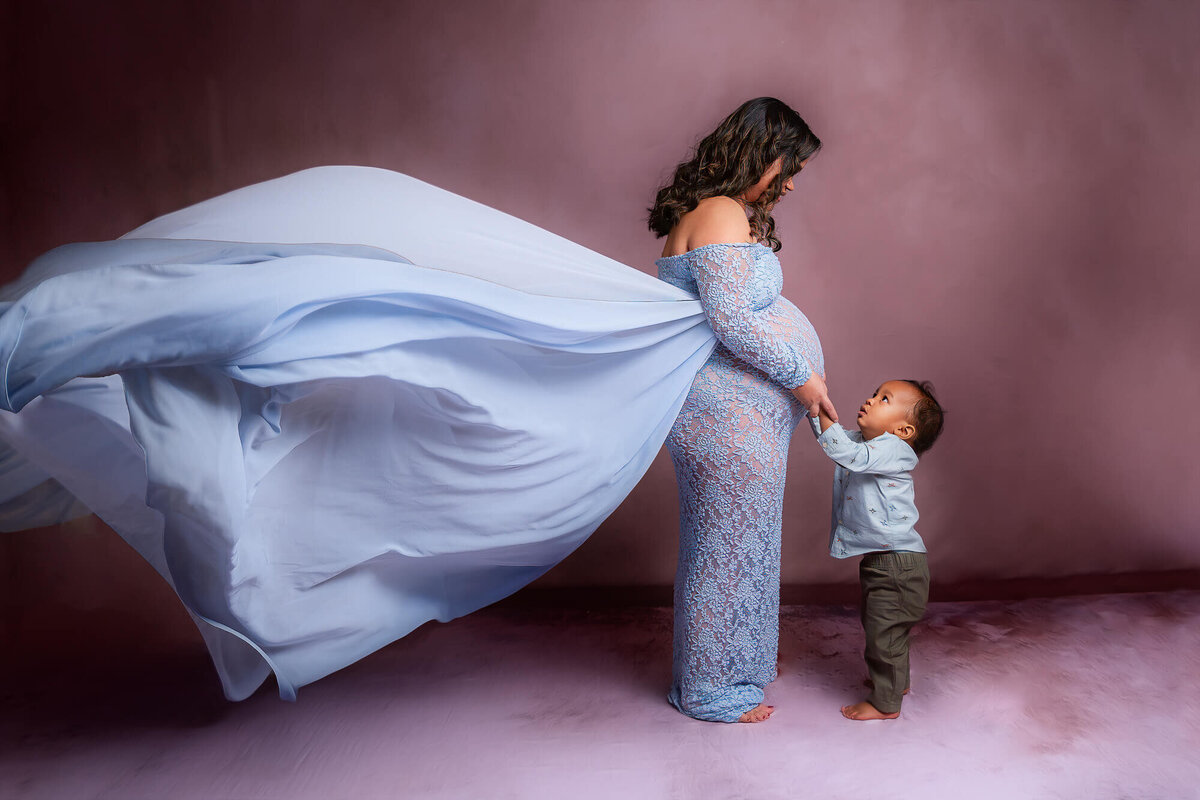 A joyful moment captured in Youngstown, Ohioof a pregnant woman in a blue dress with her son, both radiating happiness.