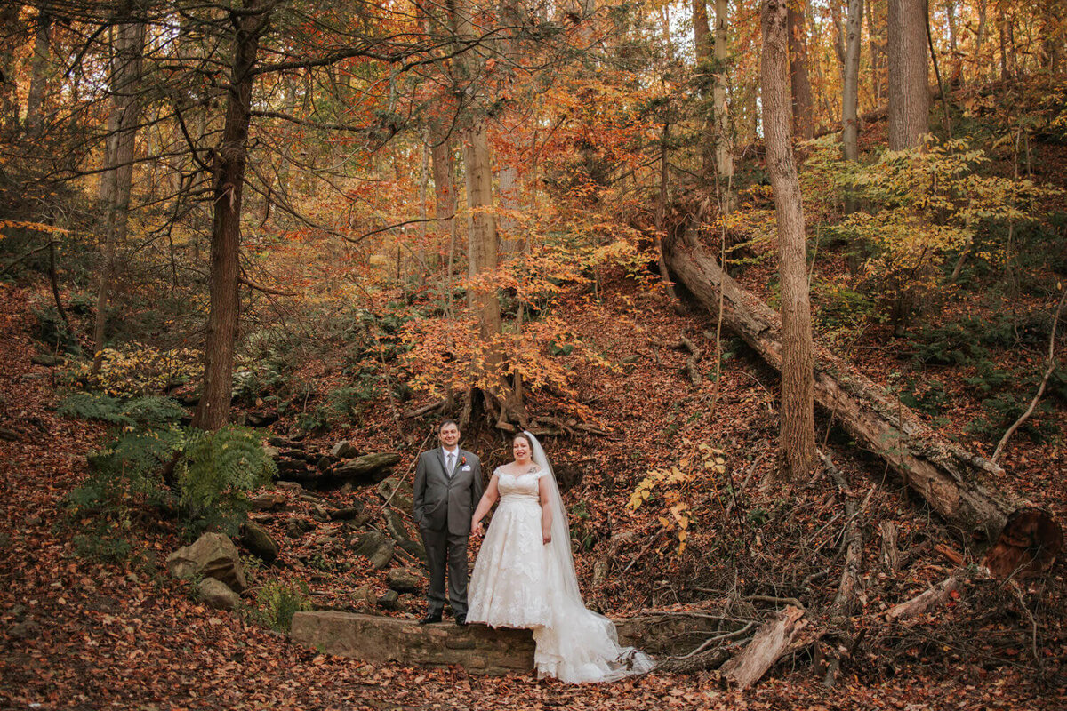 A couple stands in wedding attire amidst a serene autumn forest at Valley Green Inn, Philadelphia