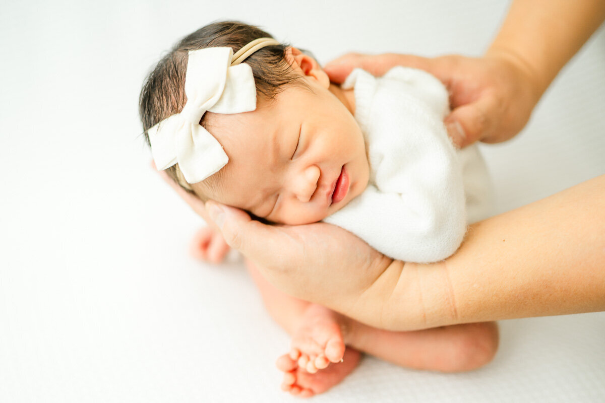 an infant girl rests her body in her father's hand while sat on a white bean bag for her infant photography session in Austin. 