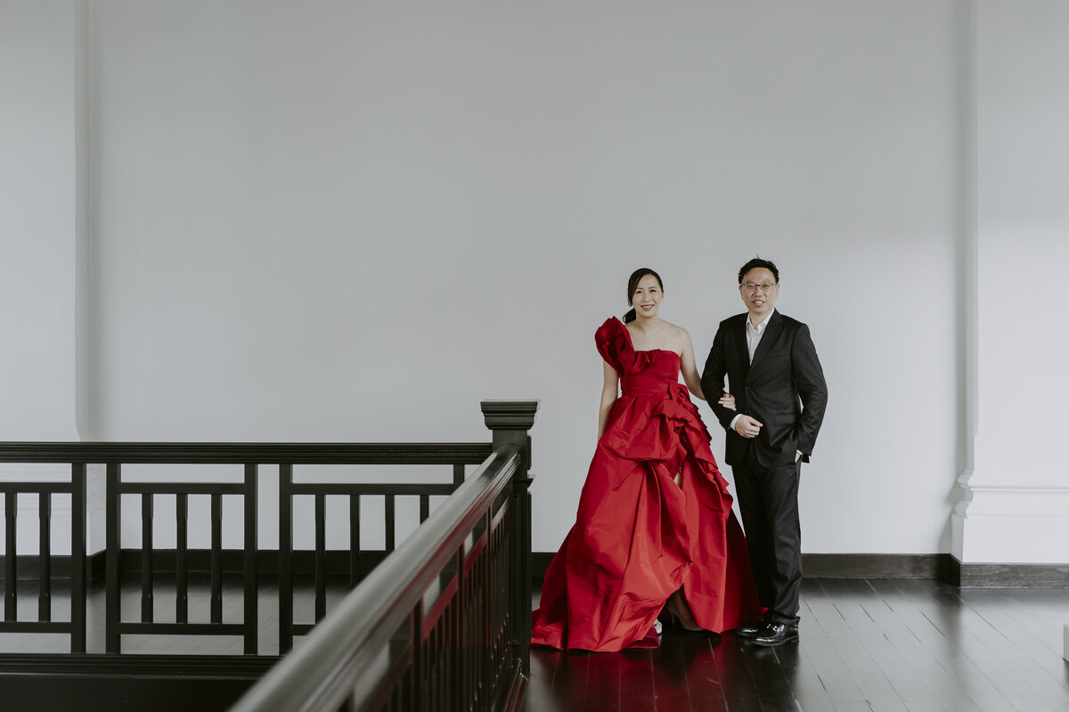 bride wearing a red cheongsam dress and the groom wearing a black suit pose on the balcony of the raffles hotel