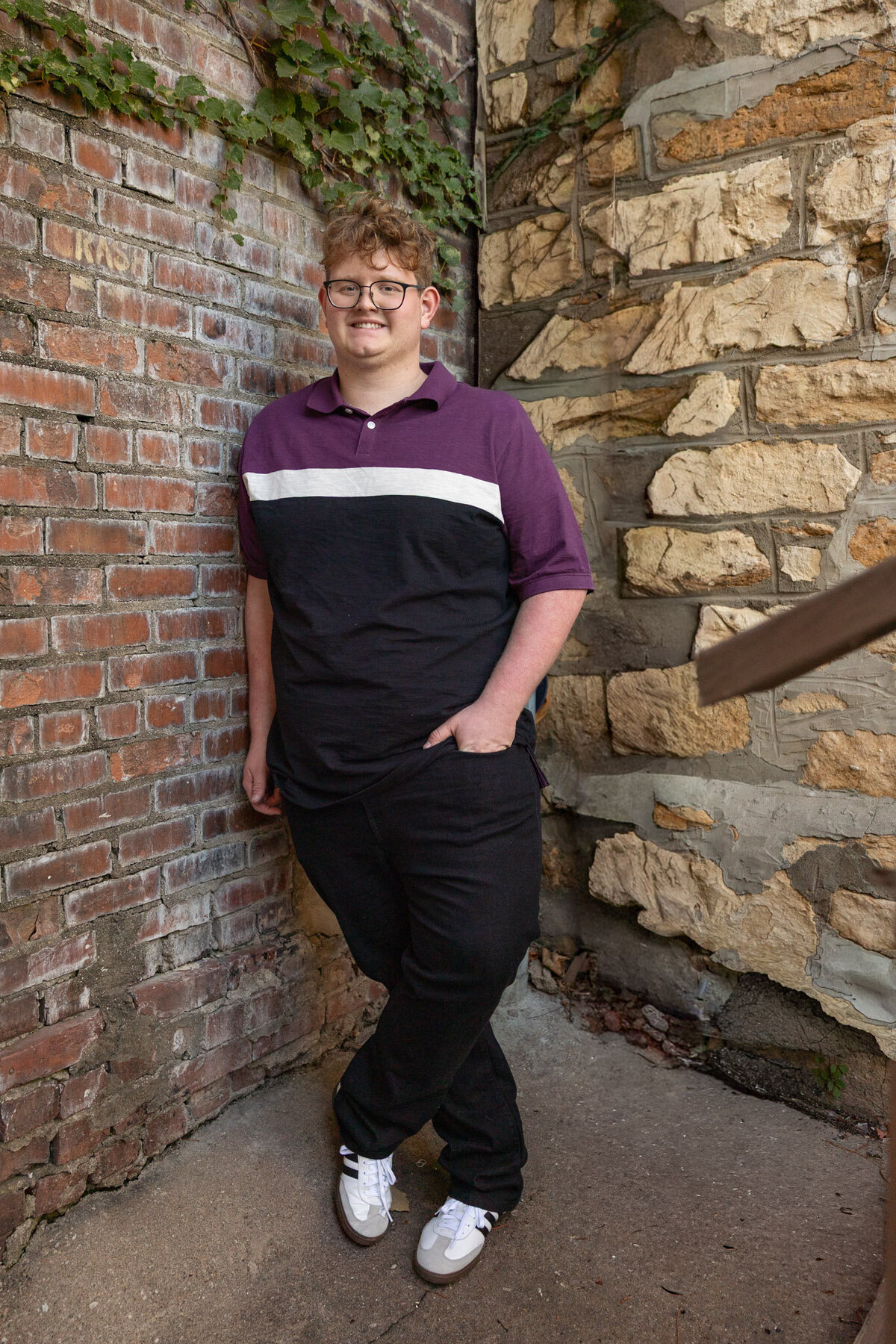 A senior guy leaning against a brick wall with a hand in his pocket in Lawrence, KS
