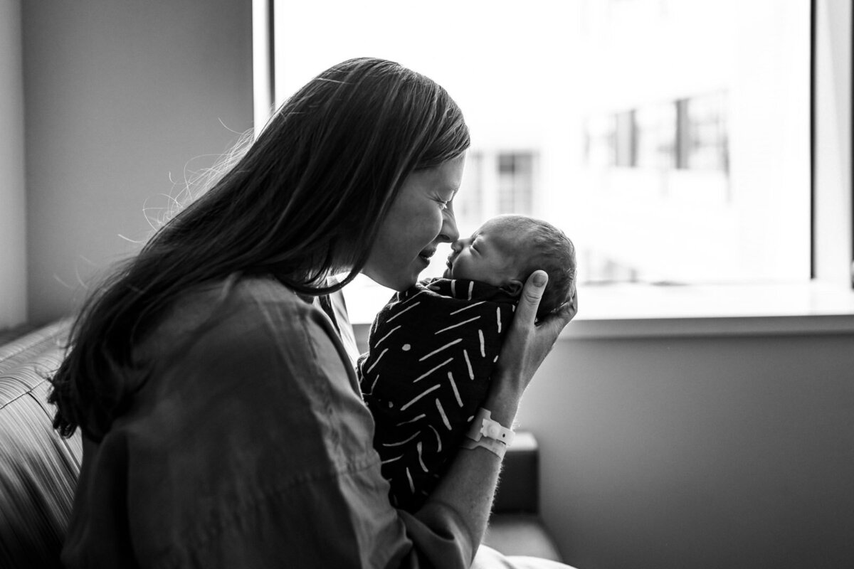 mom holding swaddled newborn to her nose while sitting on hospital couch
