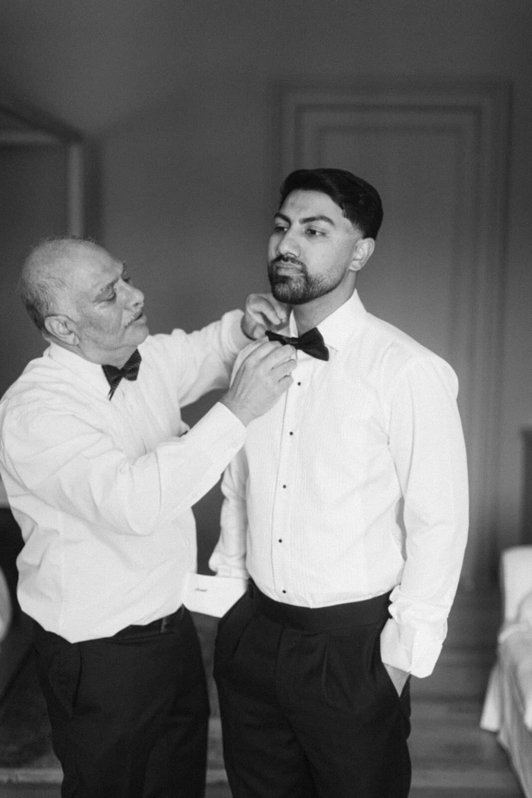 Father adjusting the groom’s bow tie in a touching pre-wedding moment, by Paris wedding photographer Thomas Raboteur