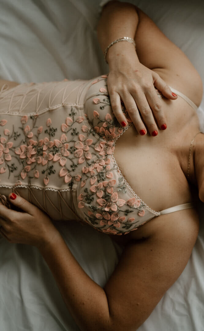woman wearing tan bodysuit lingerie with hand on chest