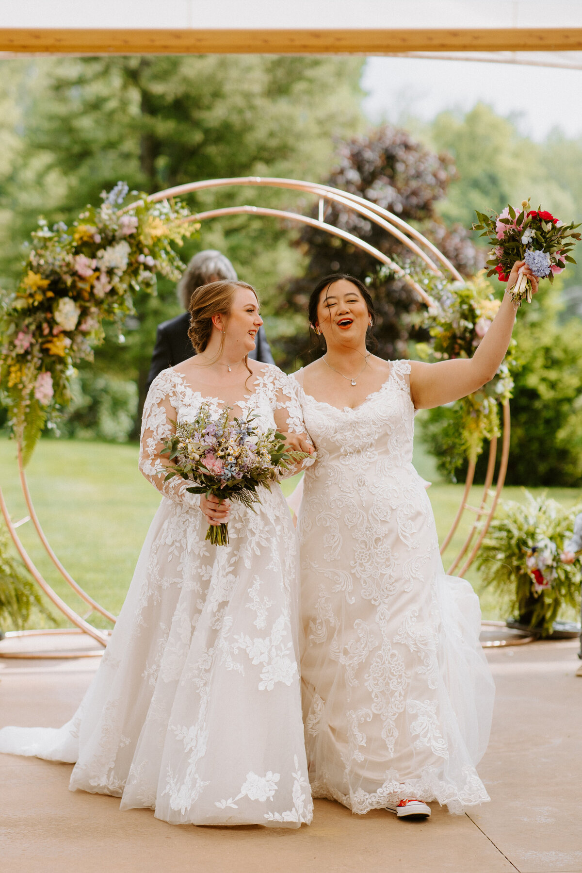 two brides with their arms linked walking up the aisle