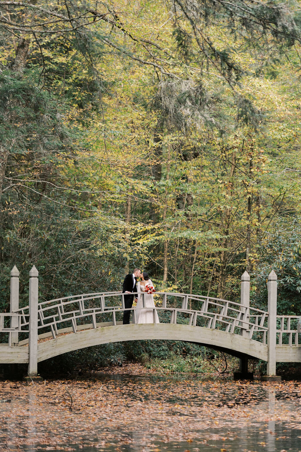 Bride and groom share a kiss on an arched bridge over the pond at Old Edwards Inn in Highlands, North Carolina.