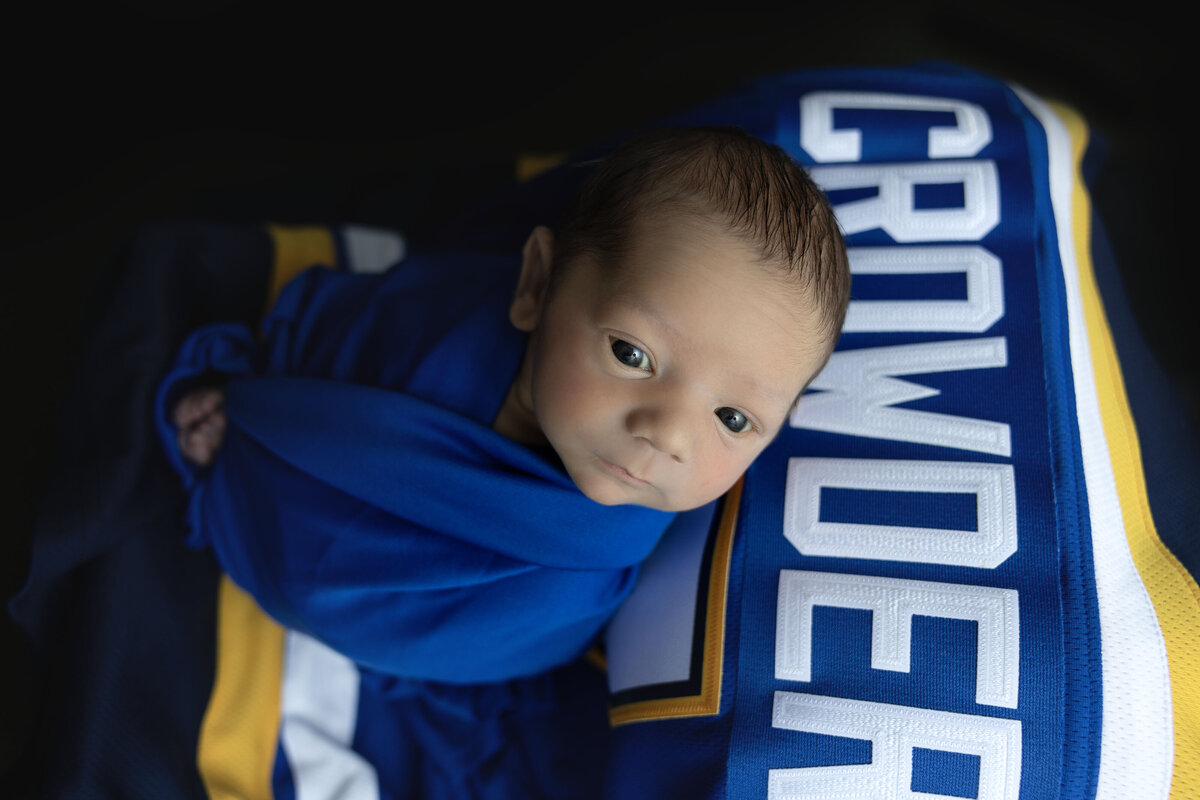 A newborn baby lays swaddled on top of a St. Louis Blues Hockey Jersey.