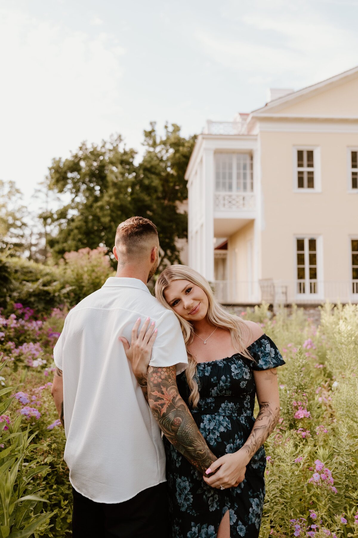 Pregnant woman embracing her partner from behind in a garden filled with flowers at the Home of Franklin D. Roosevelt in Hyde Park, captured by a Hudson Valley maternity photographer.