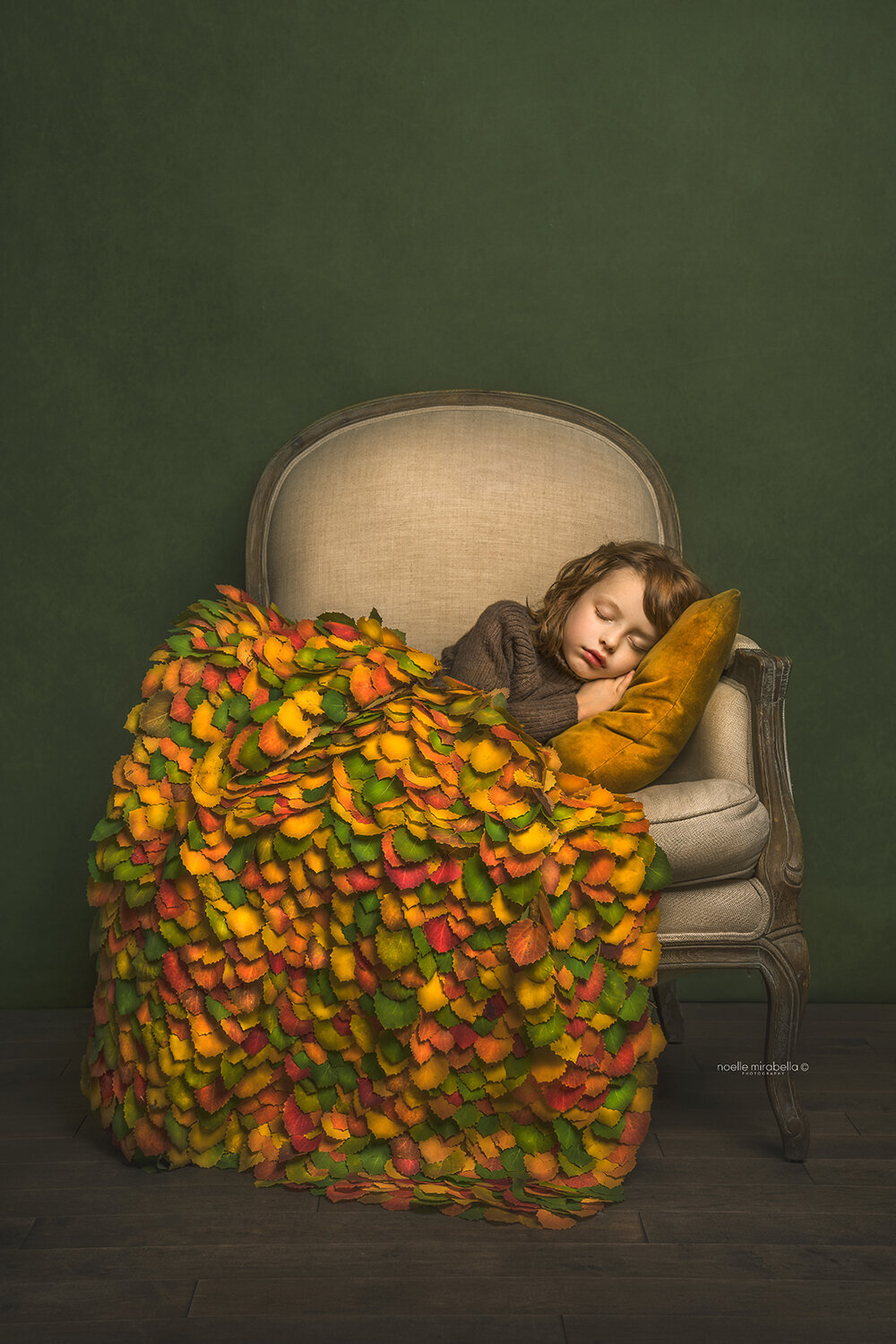 Child sleeping in chair covered in a blanket made out of leaves.