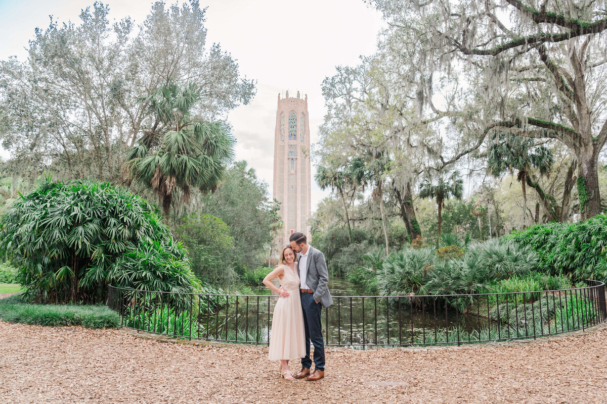 Couple standing in a lush garden with a tall stone tower at Bok Tower Gardens