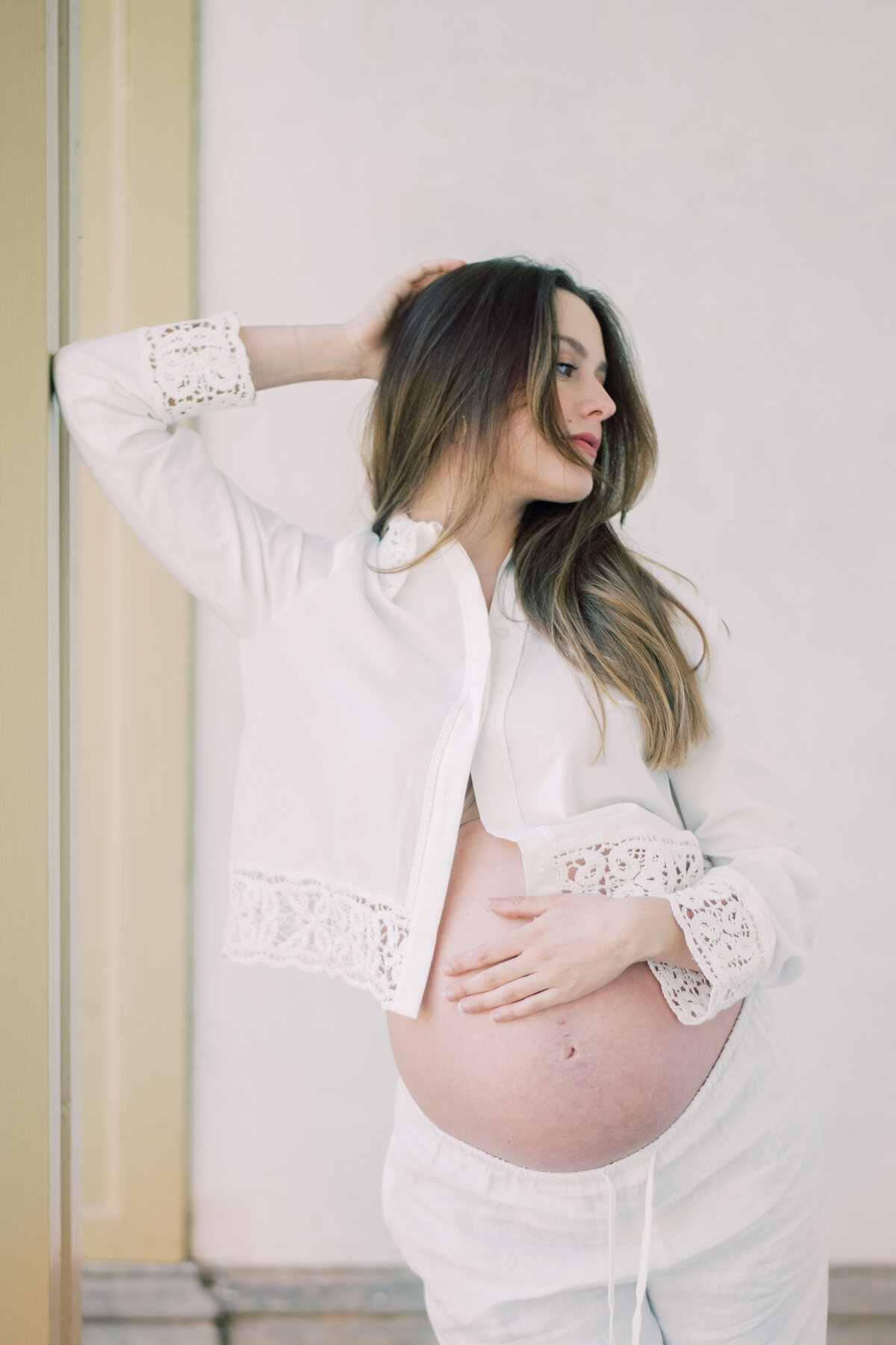 Softly lit color image of a pregnant woman embracing her belly, styled in all-white Zara pieces
