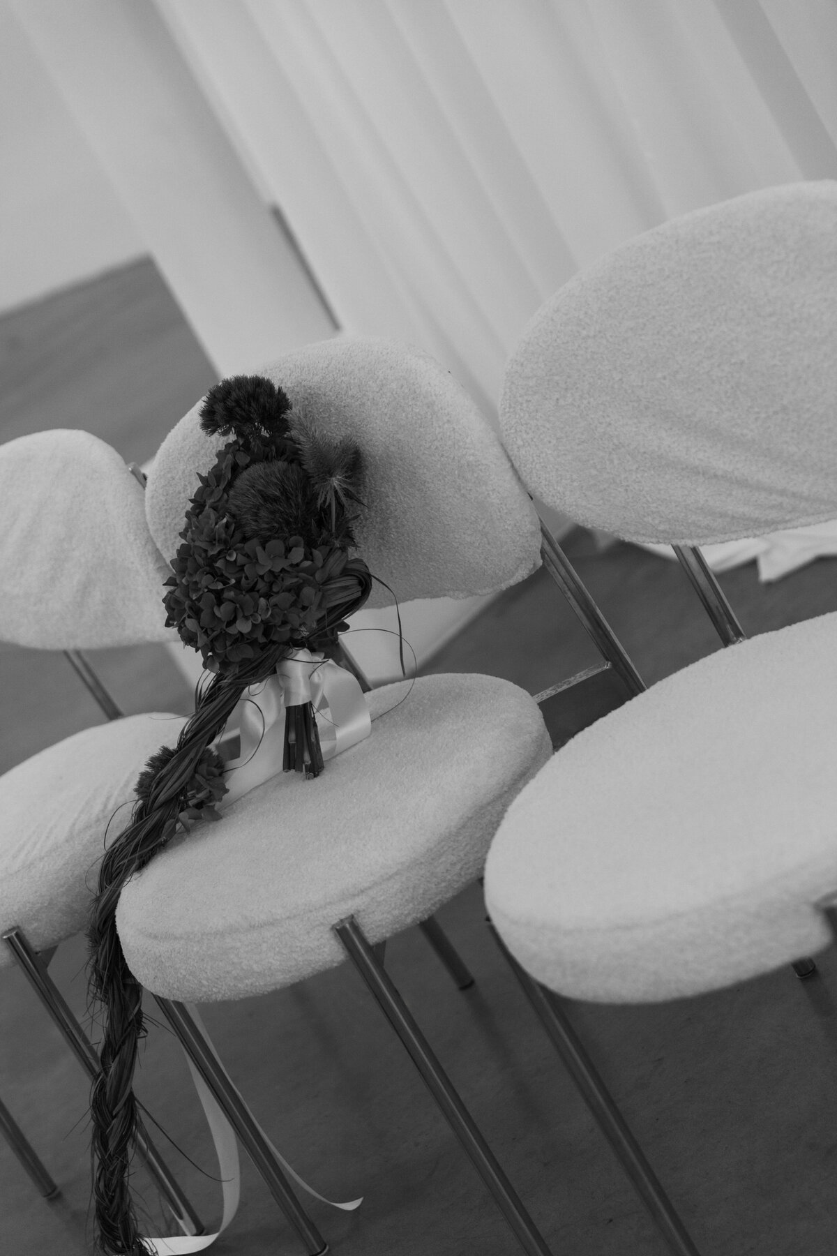 Black and white photograph of a wedding bouquet placed on a modern white ceremony chair during an NYC editorial shoot.