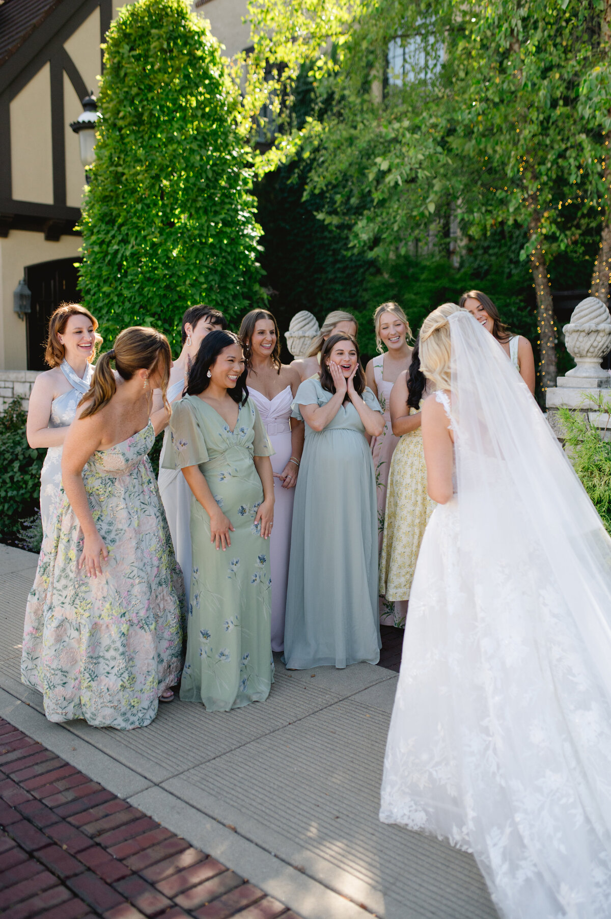 Bride surrounded by bridesmaids in pastel dresses, sharing a joyful moment.