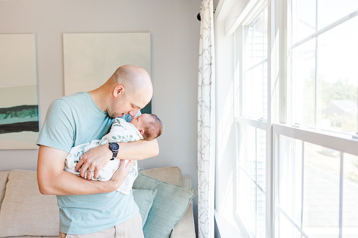 father holds baby by window  during in home newborn photo session with Sara Sniderman Photography in Metro West Boston Massachusetts