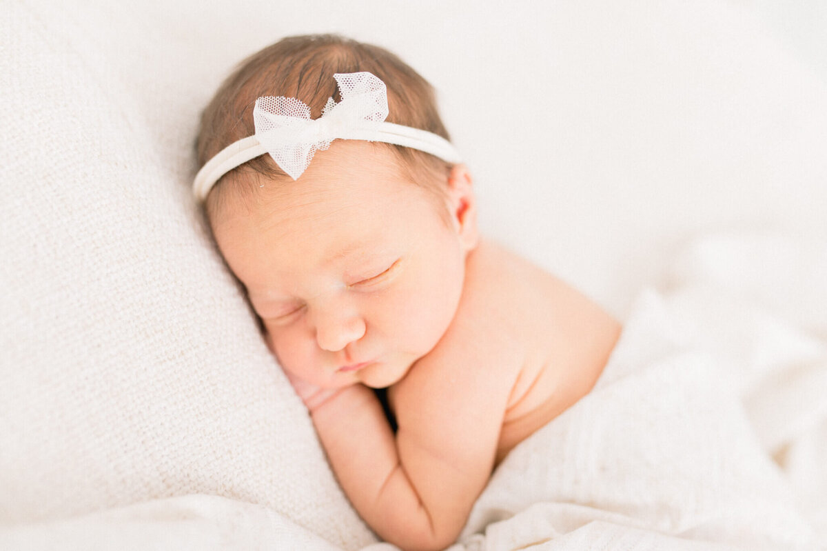Newborn laying with arm under head and swaddle around her. Captured by Niagara newborn photographer