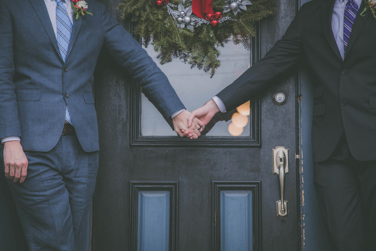 Closeup on grooms holding hands against doorway.