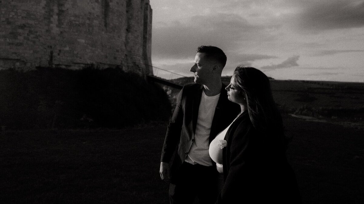 Instant suspendu pour Anissa et Brendan, regardant au loin, au pied de ruines historiques en Normandie. Photographie en noir et blanc par kamescop, vidéaste et photographe vintage.