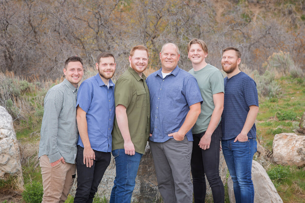 Dad and five sons wearing blue and green posing in a line at a mountain park