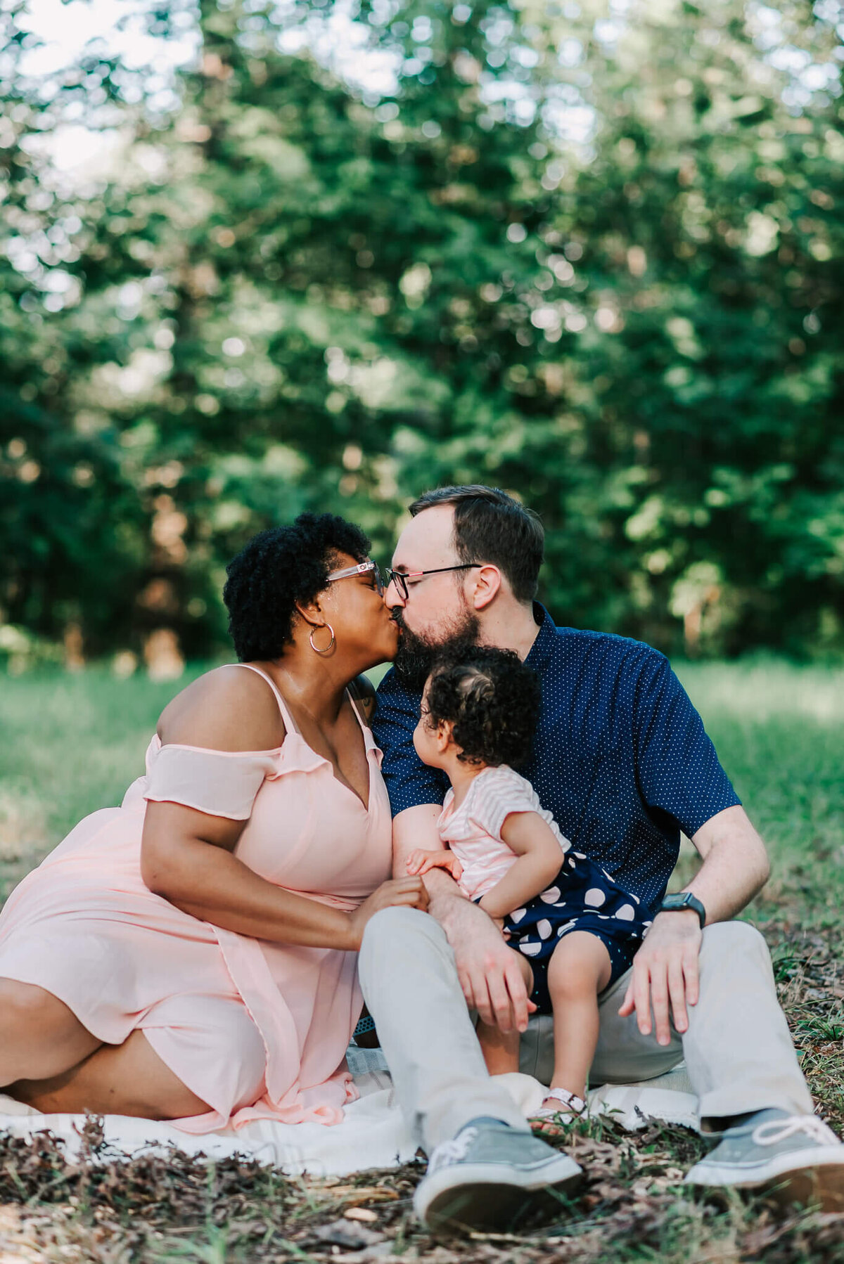Parents sharing a kiss with their daughter in his lap captured by northern virginia family photographer, Denise Van.