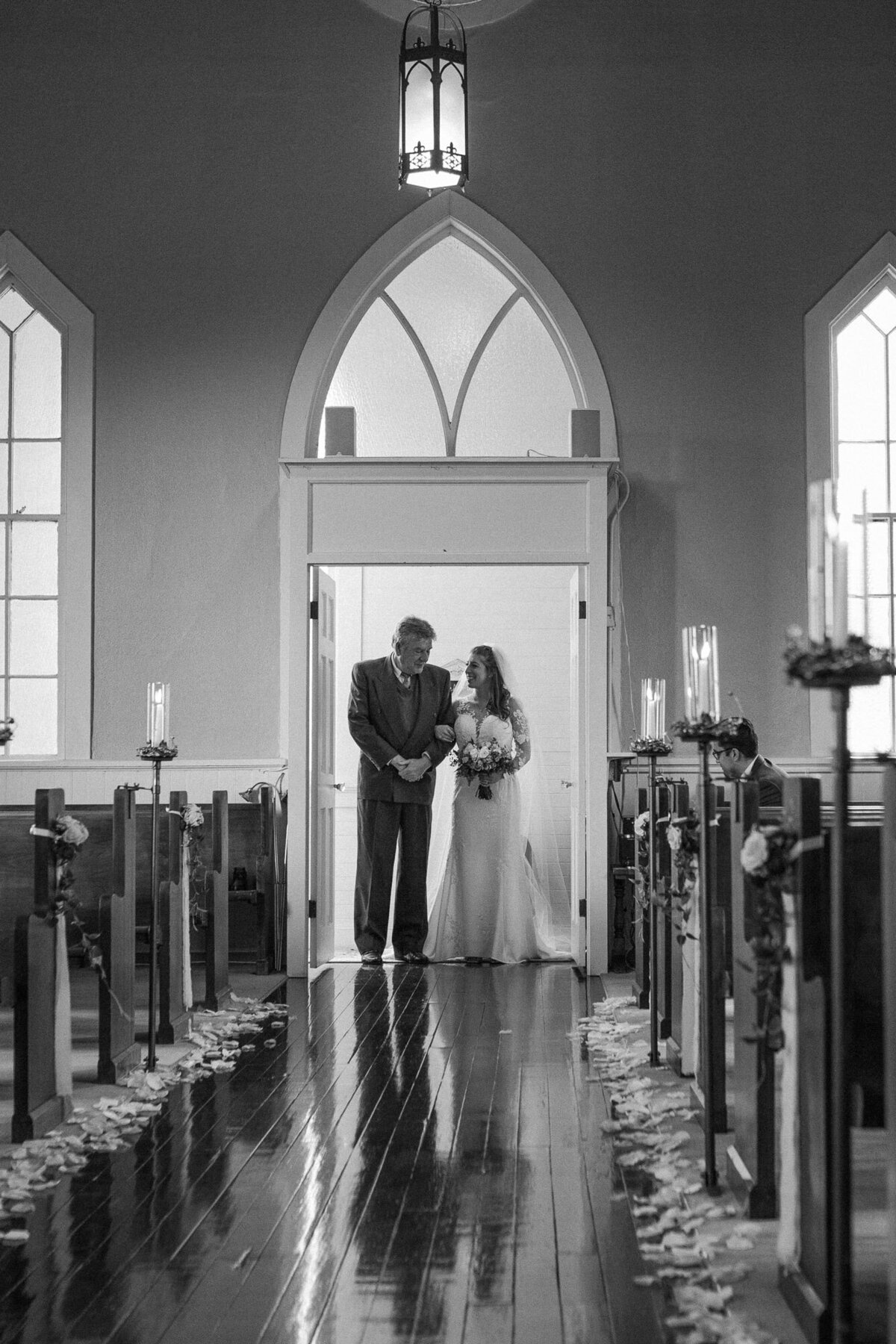 Black-and-white-photo-of-bride-and-father-walking-down-the-aisle-at-old-historic-Belle-chapel-in-Snohomish-photo-by-Joanna-Monger-Photography