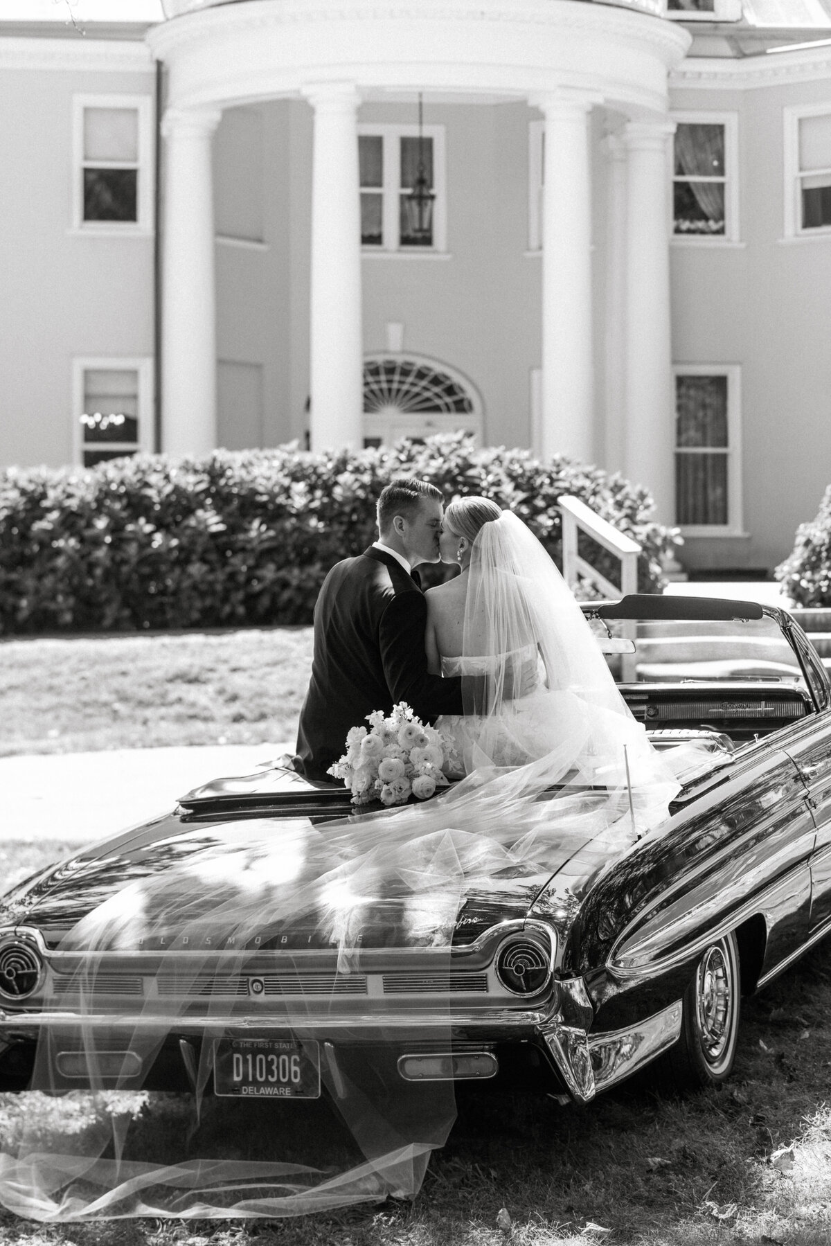 Bride and groom sitting on a vintage car in front of Bellevue Hall.