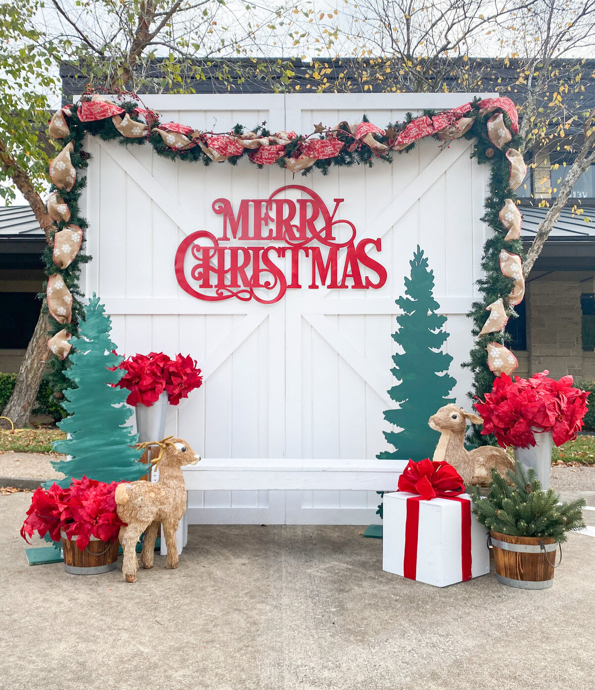 Festive Merry Christmas themed backdrop design with trees, garland, presents and red floral arrangements