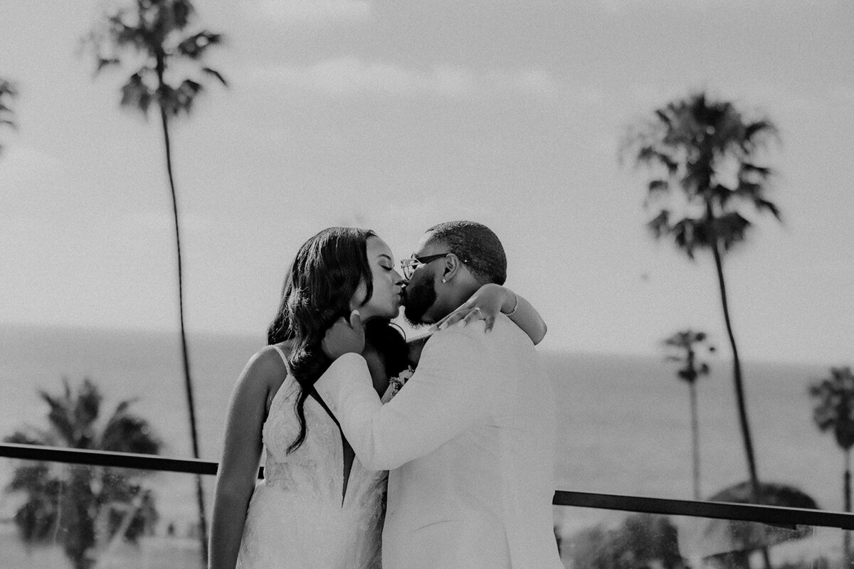Bride and groom kissing with palm trees and ocean in back in San Diego