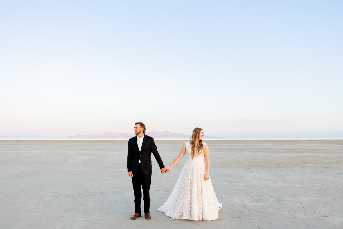 Bride and groom hold hands, facing opposite directions, against the expansive Great Salt Lake backdrop.