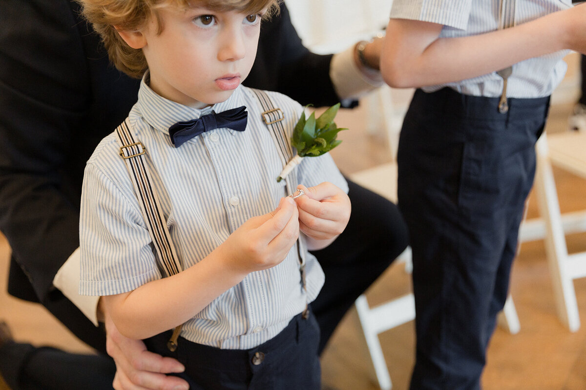 A ring bearer holds a wedding band in his fingers as he waits eagerly to be called forth to give the couple the ring.