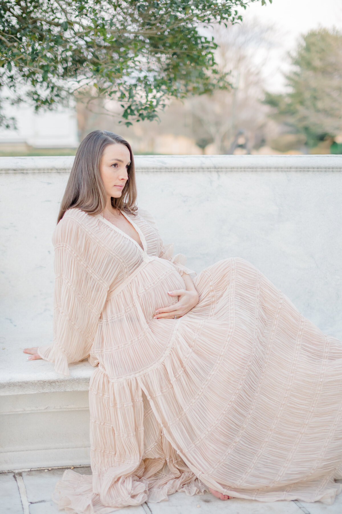Pregnant mom sitting on a bench in a quiet park, gazing lovingly at her baby bump