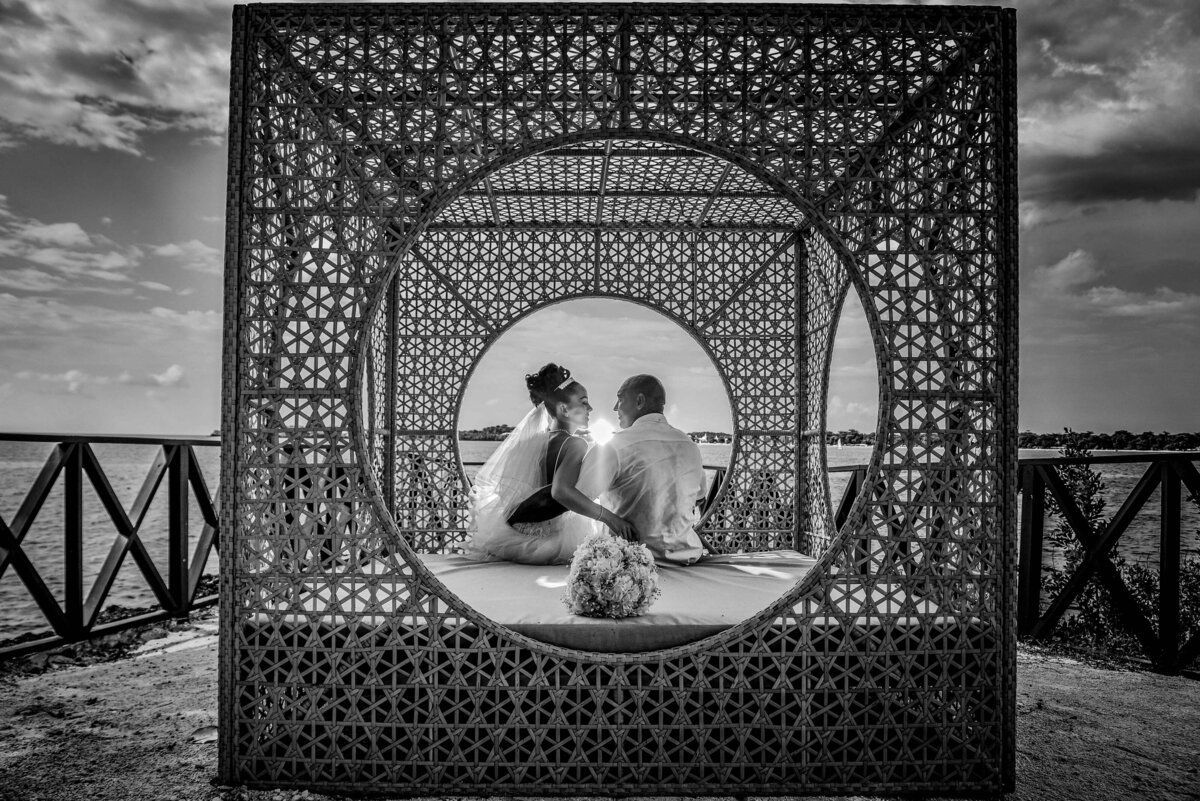 romantic bride groom sitting in tiki hut on beach bw