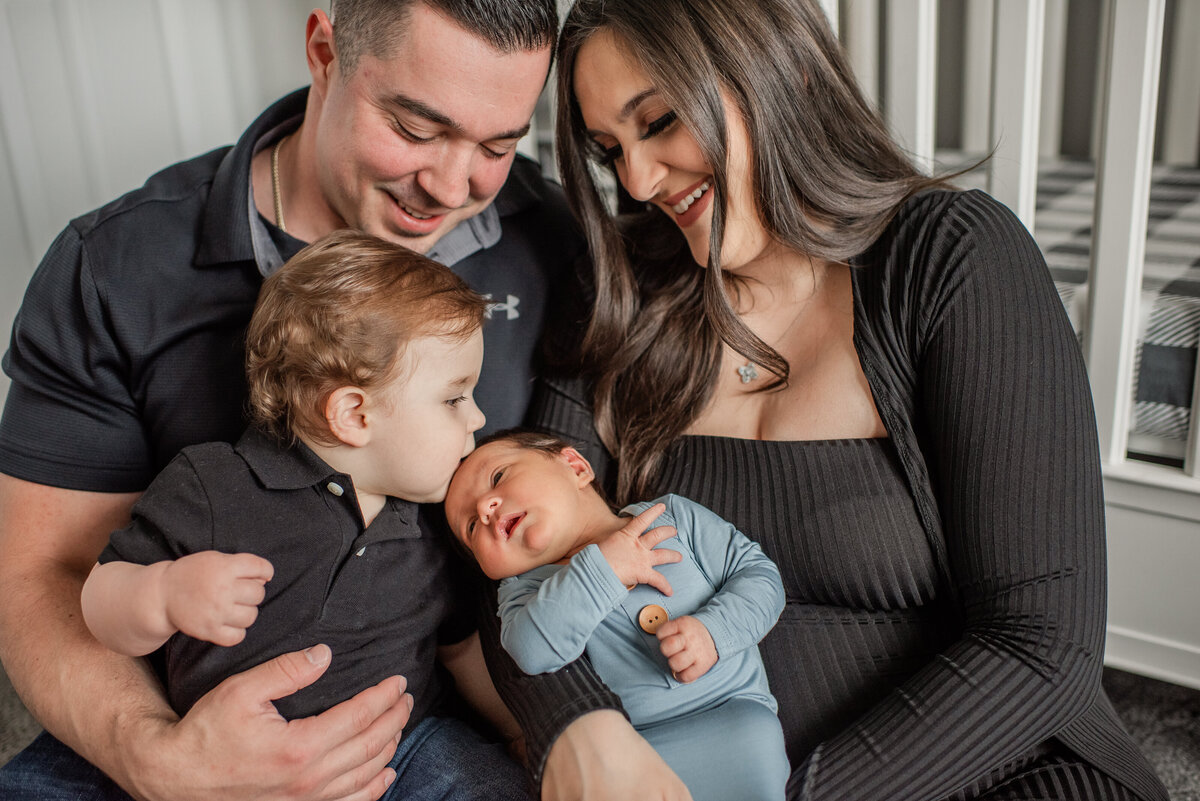 sweet big brother kisses newborn on the head while parents are overjoyed - maryland family photographer