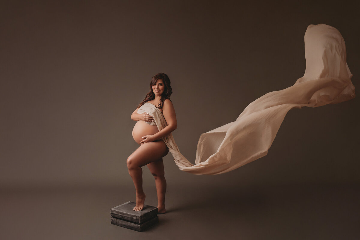 Pregnant woman at maternity and newborn studio of Atlanta posing for maternity portrait wearing flowy chiffon neutral color fabric standing