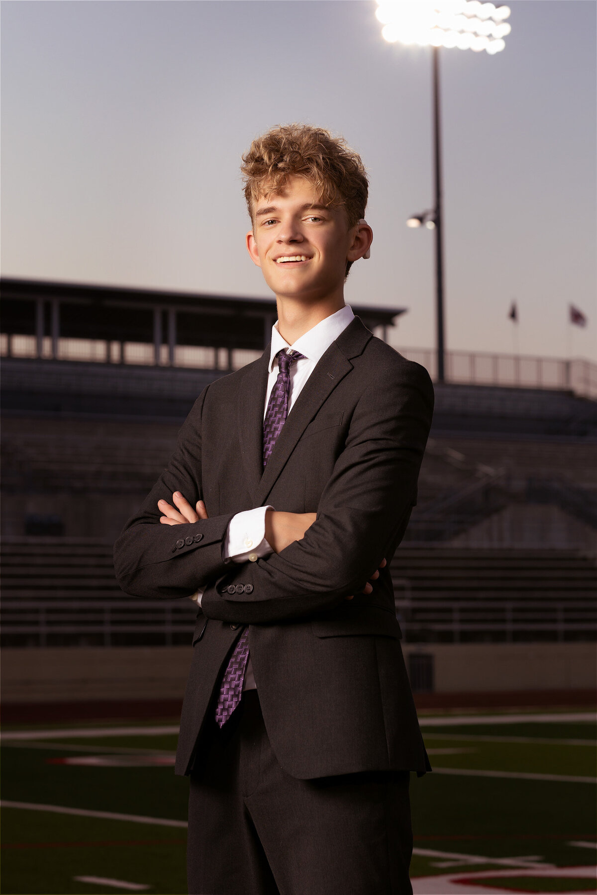 A senior in a suit smiles confidently on the football field at Mustang-Panther Stadium, captured by a Dallas senior photographer.