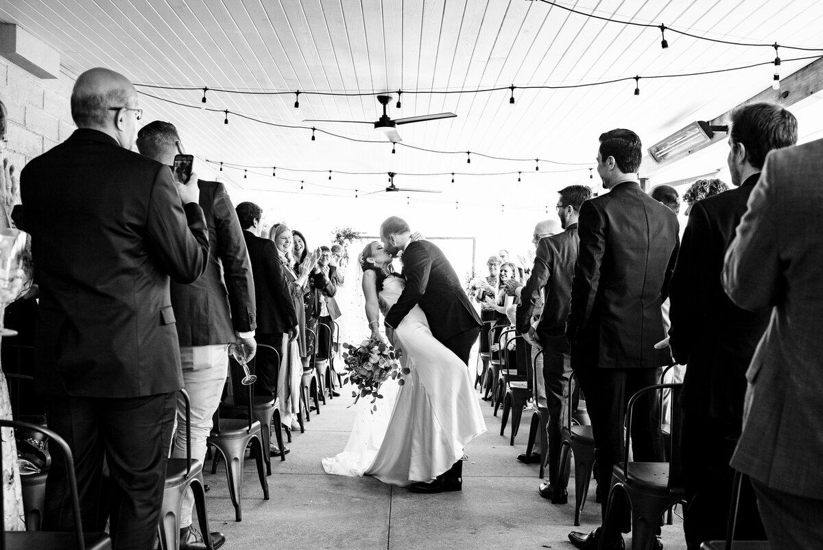 Black and white photograph of groom dipping his bride part way down the aisle at Upstairs Atlanta by Charlotte wedding photographers DeLong Photography
