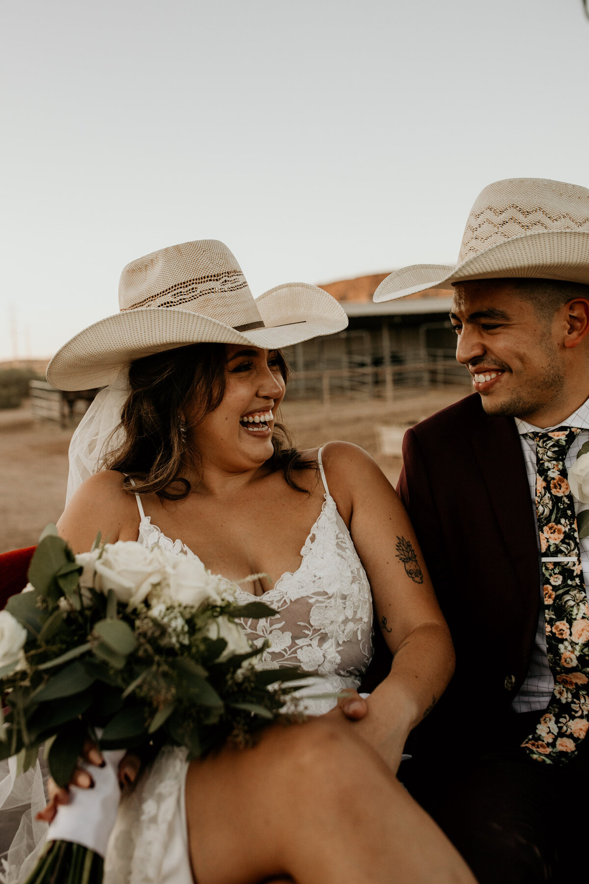 bride and groom sitting in a horse carriage with cowboy hats laughing