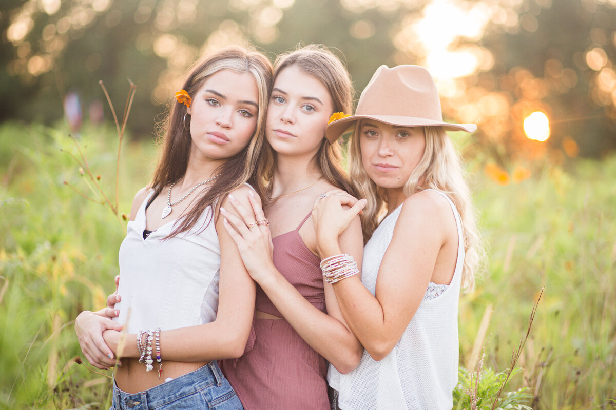 Three senior girls pose closely in wildflower field for senior session in Ridgeland, MS.