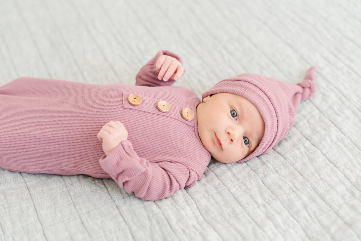 Baby in pink onesie and hat laying on white blanket - Washington DC Newborn Photographer