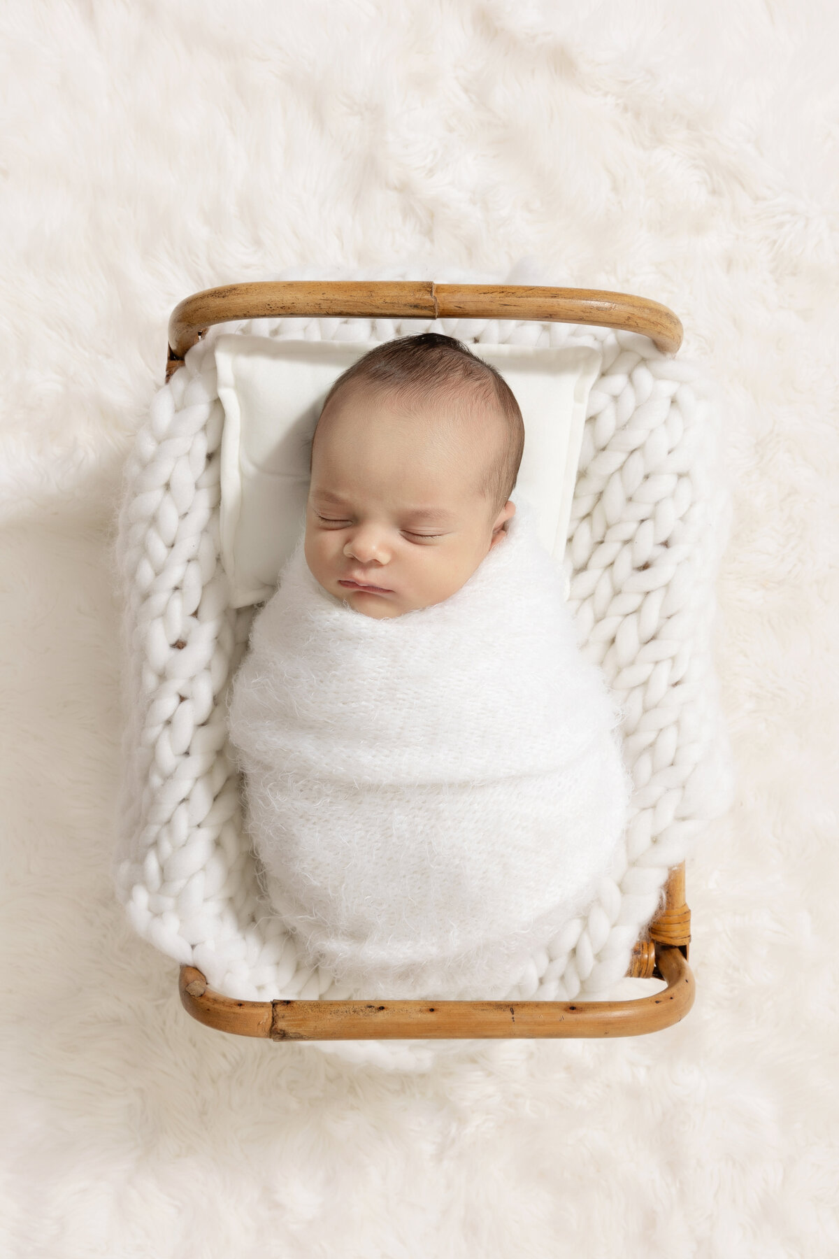 A look down at a newborn baby sleeping in a white swaddle in a wicker crib