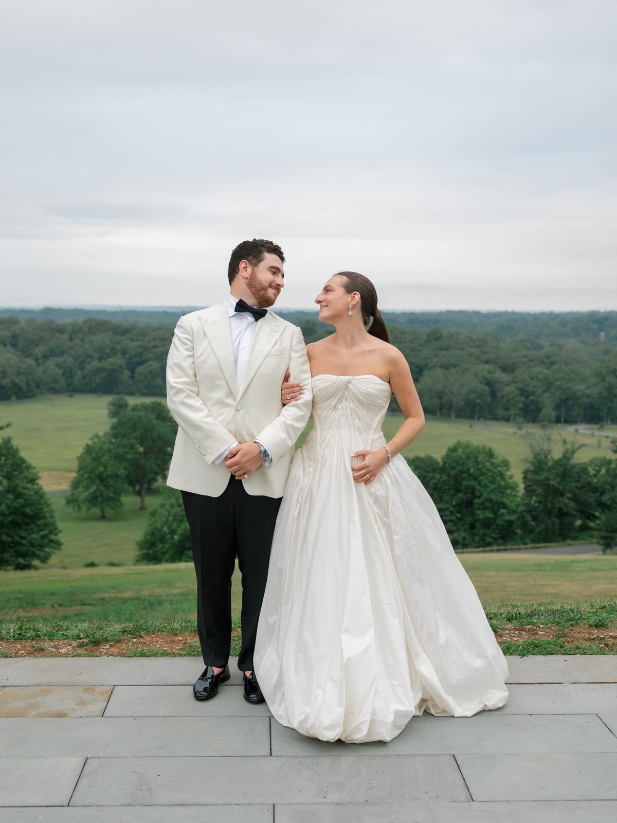 Nick in an off-white tuxedo jacket with Kara on the terrace overlooking the Natirar hills