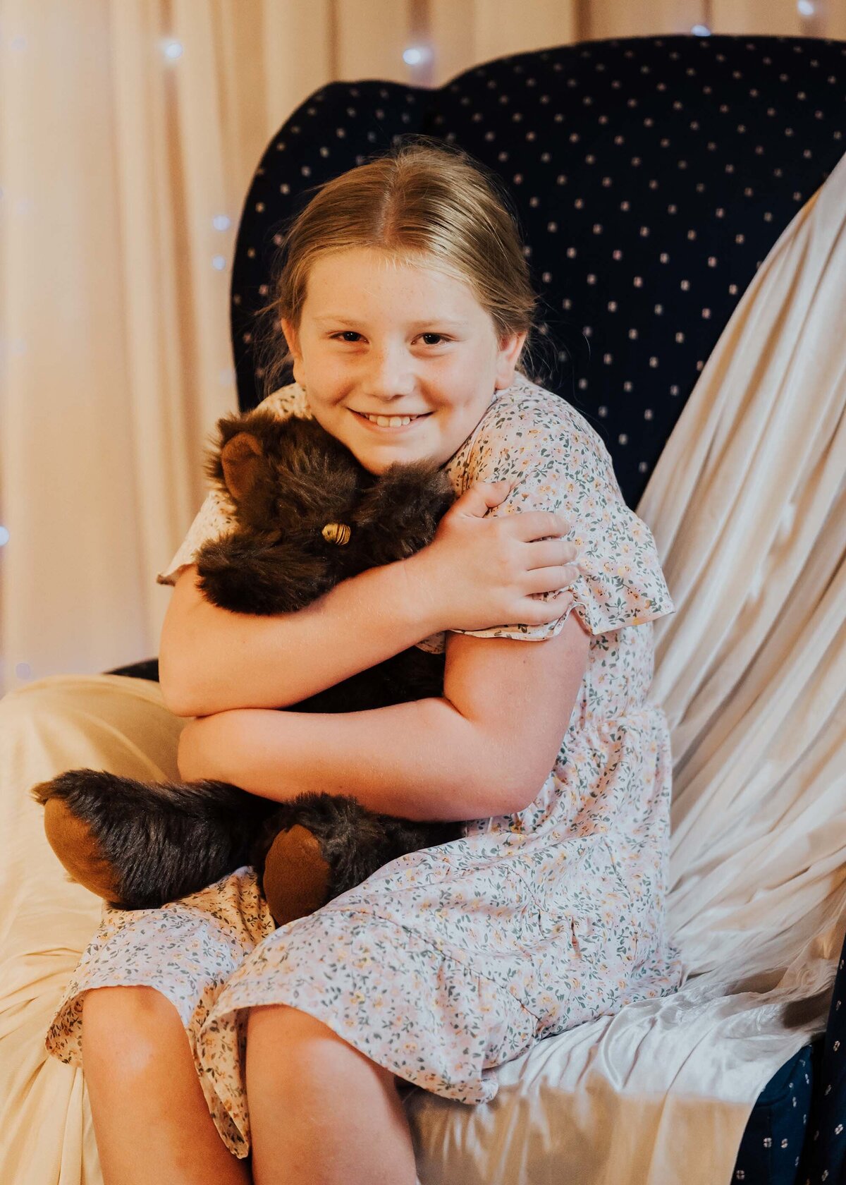 Maddie Rae Photography little girl sitting in a chair hugging a teddy bear smiling at the camera