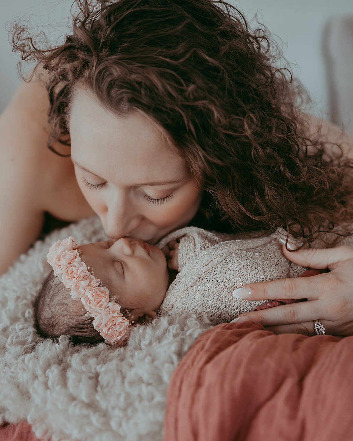 curly haired mom kisses her sleeping newborn