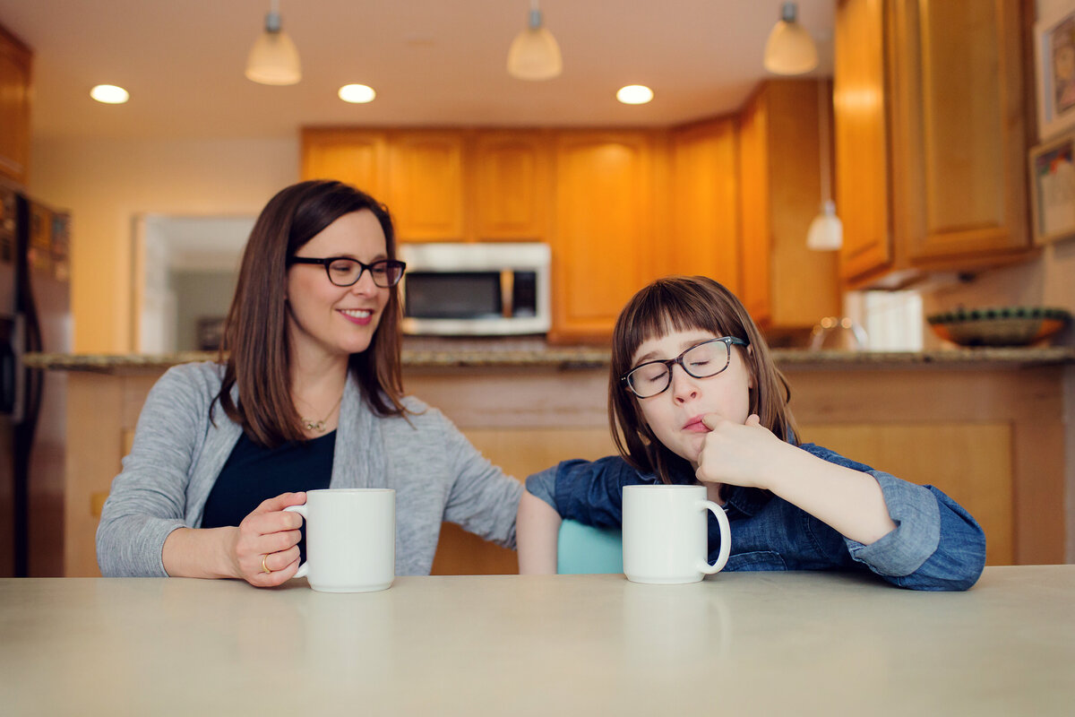 Mom watches happily as her daughter licks hot chocolate off her finger after snow time.