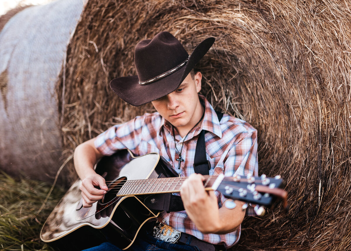 High School Senior playing guitar in front of hay bail by Lisa Smith Photography