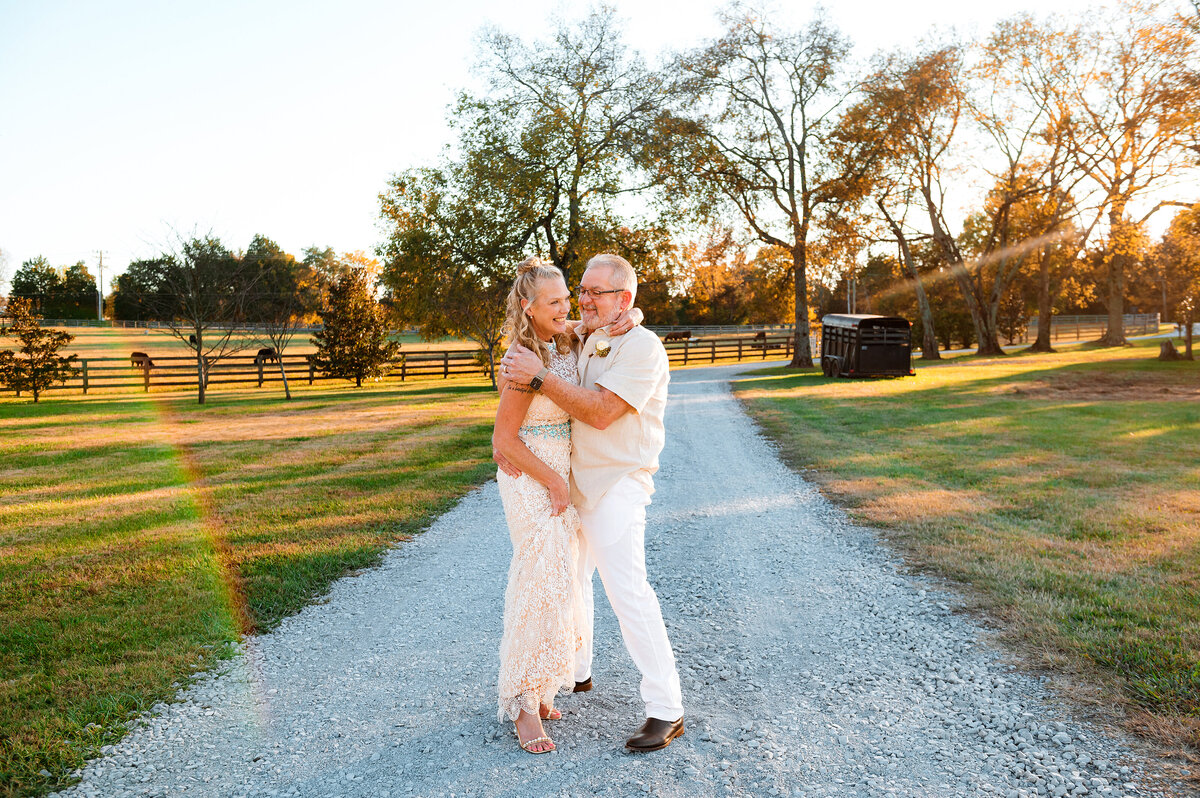 newlyweds walking on gravel road laughing during sunset