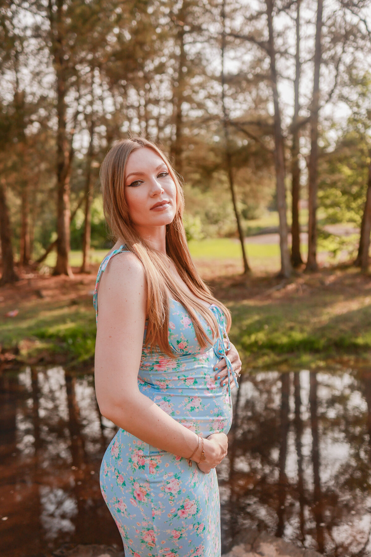 pregnant woman holding her belly wearing a blue dress with pink flowers at sunset